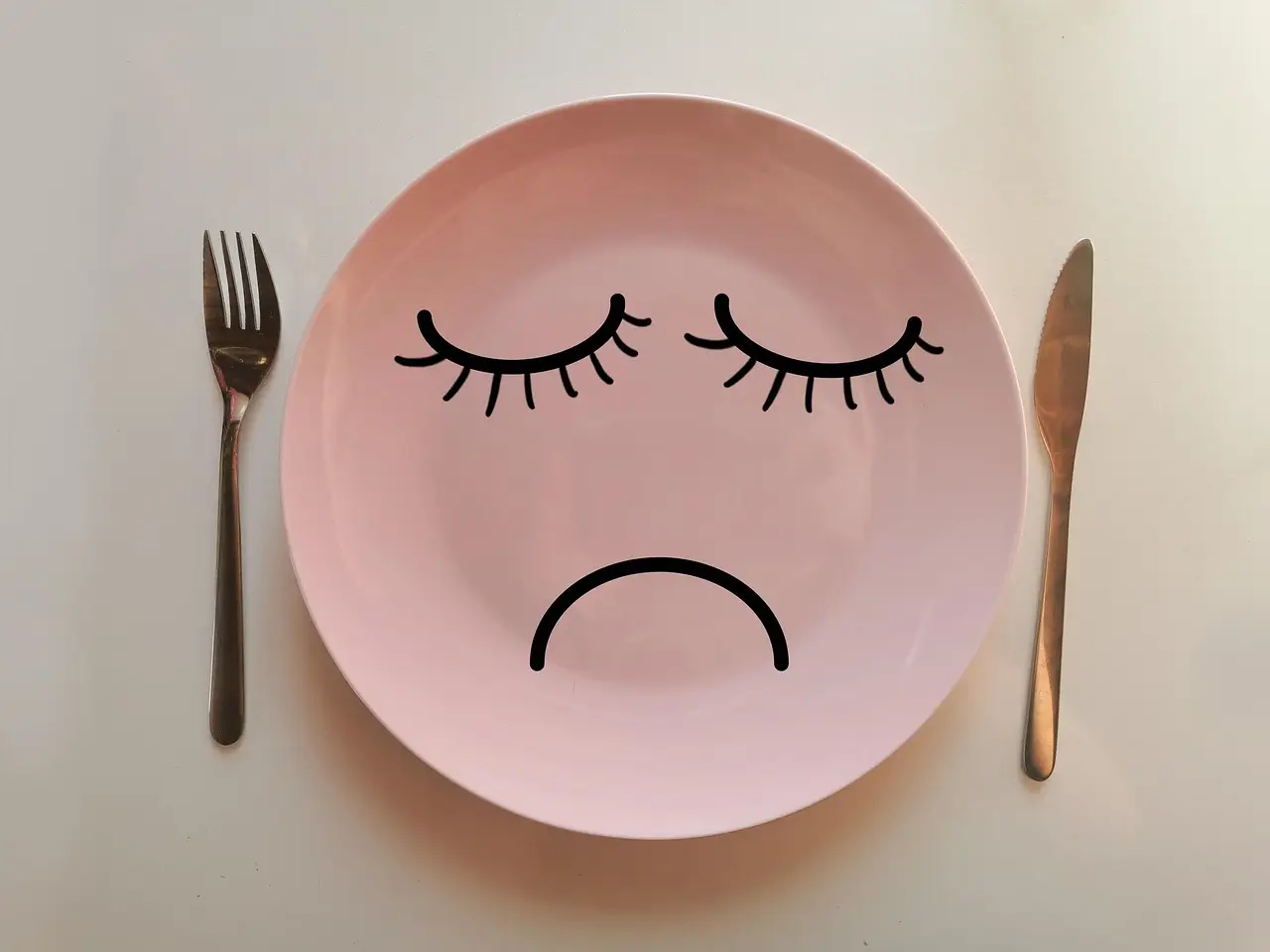 assiette rose avec une bouche et des yeux, posée sur une table accompagnée d'une fourchette et d'un couteau. Les bienfaits de l'hypnose dans une perte de poids durable.