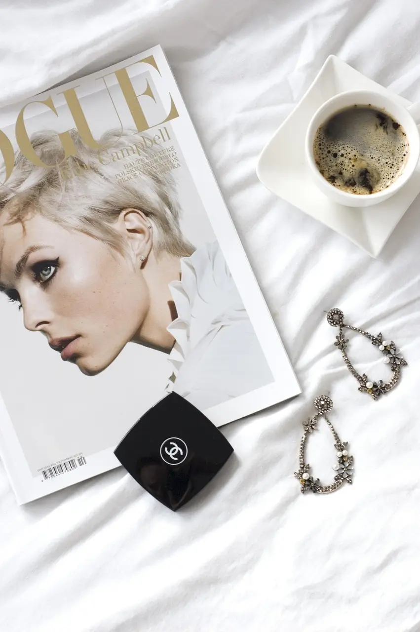 Portrait d'une femme blonde illustrant le magazine Vogue, posée sur un lit, à côté d'une paire de boucles d'oreilles en or et d'un poudrier Coco Chanel. Pourquoi l'apparence physique obsède-t-elle ? Le culte de la perfection et la pression du poids.